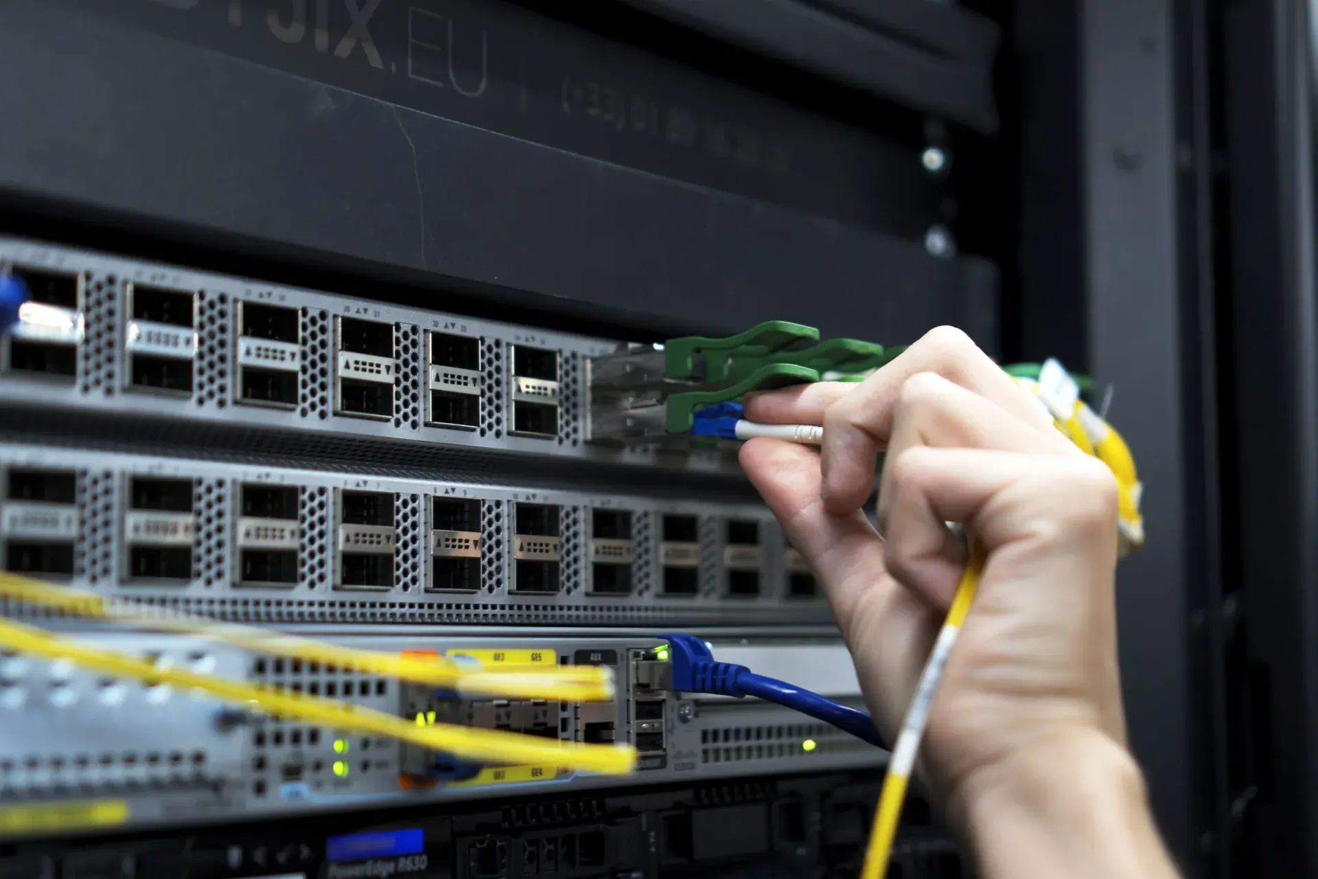 Une main raccorde une jarretière optique sur un port SFP+ d’un commutateur Dyjix